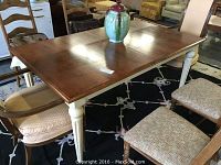 View of rectangular dining table with wooden top and white painted legs, showing scratches and wear on leg