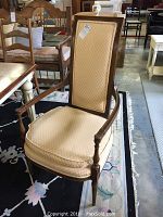 Single armchair showing front and side with carved wood frame and beige patterned upholstery on cushioned seat and back