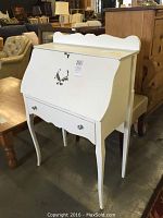 Front angled view of white drop front secretary desk showing silver-toned drop front handle and drawer pulls, curved legs, and scalloped edges.