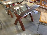 Side angle view of the beveled glass side table showing wooden X-shaped legs and clear glass top.