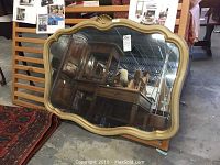 Full view of the tan wood framed mirror showing scalloped edges and reflective glass.