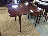 Full view of antique wooden card table open with visible polished surface, carved legs, and wheels.