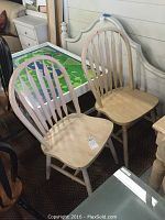 Two wood dining chairs showing natural finish, rounded vertical slat backs, and contoured wood seats, showing wear such as chips, scratches, and scuffs.