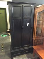 Full exterior view of the closed black gun cabinet standing next to other furniture pieces.