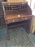 Front view of wooden roll top desk showing two drawers with white porcelain knob handles, and eight upper open compartments for storage. Visible wear, chips, and scratches on wood.