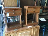 Two matching wooden side tables with two drawers each and open shelves below showing wear, chips, and scratches on surfaces.