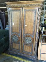View of wooden armoire desk front showing carved floral medallions on double doors and ornate trim and handles.