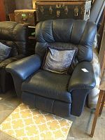 Front view of blue leather reclining chair with detached footrest and decorative cushion placed on seat. Chair is plush with padded segmented back and armrests.
