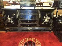 Front view showing entire black lacquered cabinet with floral inlay and metal handles on a red carpet.