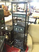 Front view of black wooden organizer with mother of pearl inlay, showing cabinets and shelves in furniture showroom.