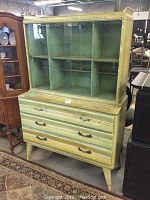 Front view of green mid century china cabinet showing glass sliding doors on upper portion and drawers below.