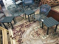 Wide angle showing three green metal outdoor side tables on a floral carpet in an indoor setting.