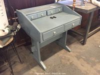 Blue wooden desk from an angle showing left side and front. Desk has four drawers with white round knobs and a slanted writing surface.