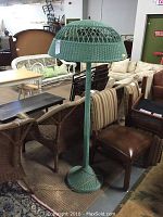 Full view of turquoise wicker lamp standing among other furniture items, showing the base, pole, and lampshade shape.