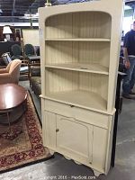 Full view of cream painted corner hutch showing shelves, drawer, and cabinet door