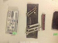 Multiple socket sets with accessories laid out, case with worn latch visible, combination wrenches on pouch.