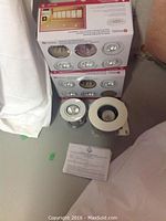 Two boxes of Utilitech GU10 white gimbal kit lights with 4 units visible each and two recessed light fixtures (4" and 5" diameters) on floor alongside instruction sheet.