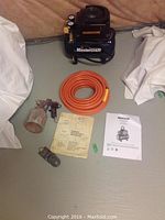 View of entire lot including Mastercraft air compressor, orange air hose, spray gun, and user manuals on floor surface.