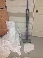 Full view of the Shark steam mop standing upright next to a door with five cleaning pads laid on the floor.