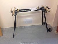 Full view of black metal extendable mitre saw stand with wood supports, showing height and width.