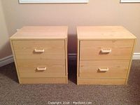 Front view of two matching laminated particle board night stands, each with two drawers and light wooden finish.