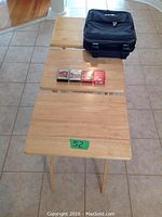 Three fold-up TV tables lined up on floor with four decks of playing cards and black wheelie travel bag with handle.