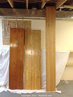 Three laminated wooden boards displayed upright, showing various wood finishes and sizes: one with a dark finish and marks, one with a lighter finish, and one unfinished.