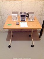Work station desk with oak finish and metal frame with caster wheels, Curtis RCD869 mini stereo with two separate speakers on top, displayed with remote and manual.