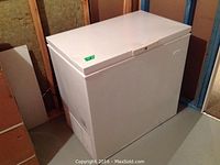 White Electrolux chest freezer with visible dent on lid, located in basement storage with surrounding wall insulation and unfinished walls.