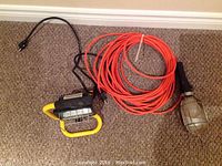 Two work lights on carpet floor: one with orange extension cord coiled, metal cage quartz light; the other smaller yellow framed light with black cord.
