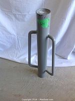 Grey steel post driver showing cylindrical body with handles from front angle.