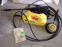 Full view of yellow Karcher K2.35 power washer with hose, wand, power brush, and manual on concrete surface.