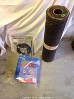 Sand blaster kit in original packaging, blue tarp, and rolled felt on floor