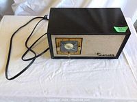 Full view of the Crosley E-90 clock radio showing black rectangular body, front speaker grille, clock face, and power cord.