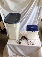 Two beige Rubbermaid containers with dark blue lids and a brown extension cord displayed on a draped cloth.