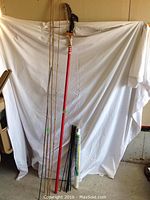 Whole lot arranged against white backdrop showing bamboo stakes of varying lengths and the long-handled tree pruner with red pole and black cutting blade.