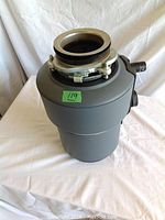 Front angle photo of InSinkerator food waste disposal unit showing mounting ring and side pipe outputs, placed on white background.