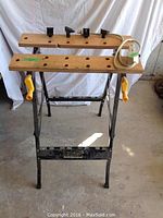 Front view of folding work table showing wooden clamp tops and power bar with cord.