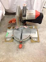 Side view of Ridgid mitre saw with blade guard, dust bag, and wooden base visible