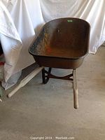 Full front view of rusty metal wheelbarrow with wooden handles, showing overall condition and basin inside.