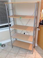 Full view of the five shelf shelving unit with metal frame and light wood particle board shelves.