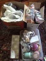 Three boxes filled with various candles, potpourri, and scented wax items visible. Some candles are in glass containers of various colors and sizes. Potpourri in plastic bags and assorted small packaged pieces also included.