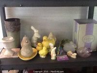 Shelf display of various ceramic and glass holiday decor pieces including ceramic chicks, bunnies, pears, and egg plate.