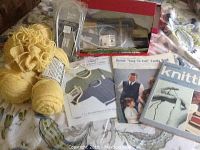 Photo of yellow yarn, knitting pattern booklets, and a knitting magazine on a floral fabric surface