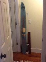 Photo showing a single vintage Viking Combi wooden water ski standing against a wall, featuring blue color with red stripes and leather straps.