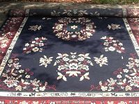 Top view of one large rectangular machine braided rug showing the floral medallion center with cream, red and green detailing on dark blue background with patterned borders.