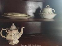 Six pieces of green and white transferware arranged on wooden shelves, including plates, a bowl, jug, and coffee pot.