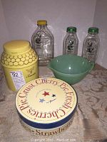 Overall view of six kitchenware items on countertop including yellow beehive sweets jar, green glass mixing bowl, Crescent Ridge milk bottles, and decorative plate lid