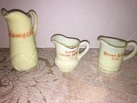Three miniature custard glass pitchers, yellow cream color with orange lettering representing Adams, Mass; Colorado Springs; and Storm Lake Iowa.