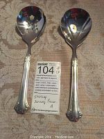 Two Reed & Barton sterling silver serving spoons on patterned cloth, showing ornate handles and distinguishing solid or slotted spoon heads.